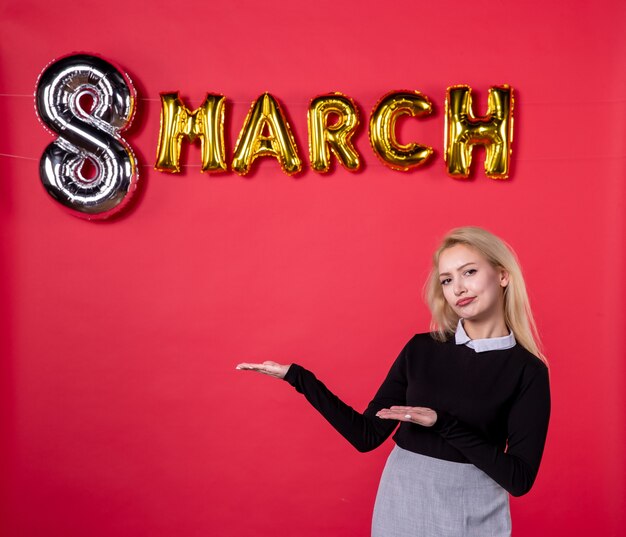 Vista frontal mujer joven con decoración de marzo sobre fondo rojo lujoso sensual igualdad femenina pasión día de la mujer día de fiesta en el salón