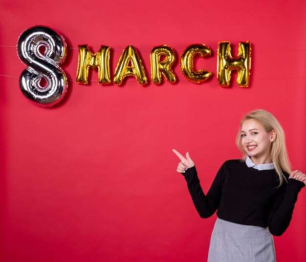 Vista frontal mujer joven con decoración de marzo sobre fondo rojo pasión salón amor día de la mujer vacaciones igualdad femenino sensual lujoso