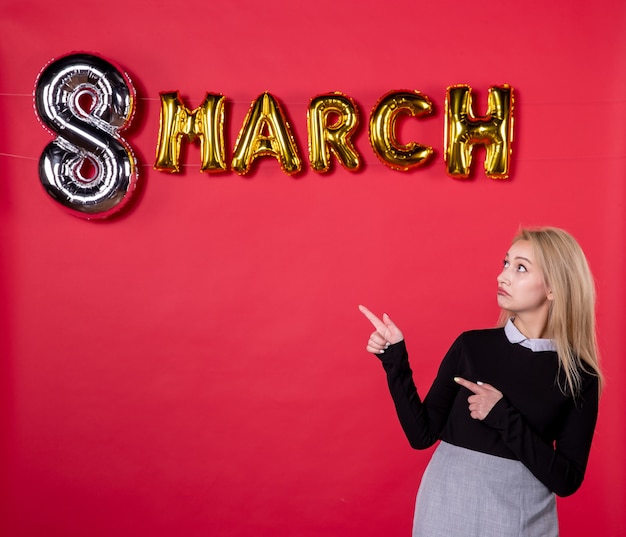 Vista frontal mujer joven con decoración de marzo sobre fondo rojo salón amor lujoso igualdad día de la mujer femenino sensual vacaciones