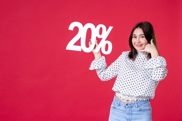 Vista frontal de la mujer joven con descuento y sonriendo en la pared roja