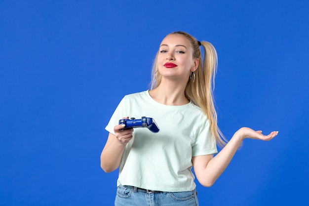 Vista frontal mujer joven jugando videojuegos con gamepad sobre fondo azul joystick juvenil adulto alegre jugador ganador en línea virtual