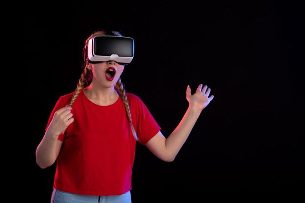 Vista frontal de la mujer joven jugando vr en la pared oscura