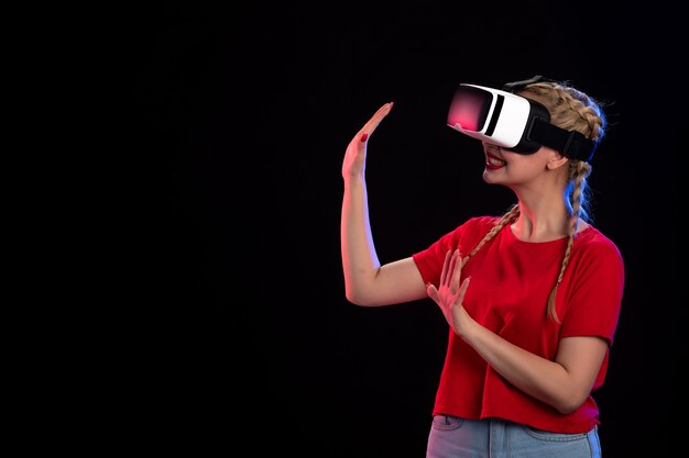 Vista frontal de la mujer joven jugando vr en la pared oscura