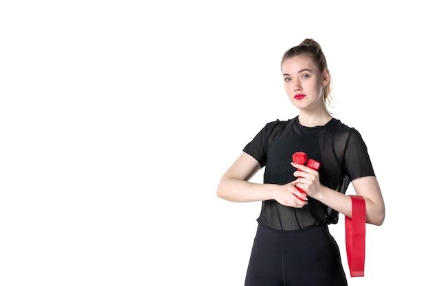 Vista frontal mujer joven con pesas rojas sobre fondo blanco gimnasio atleta deporte estilo de vida entrenamiento salud cuerpo