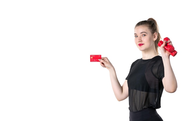 Vista frontal mujer joven con pesas y tarjeta bancaria en sus manos sobre fondo blanco gimnasio dinero atleta deporte estilo de vida salud cuerpo