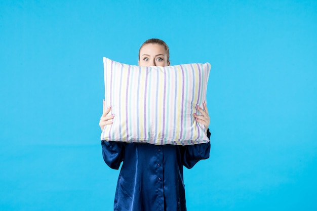 Vista frontal mujer joven en pijama sosteniendo la almohada sobre fondo azul dormir pesadilla fiesta sueño bostezo color cansado descansar cama mujer