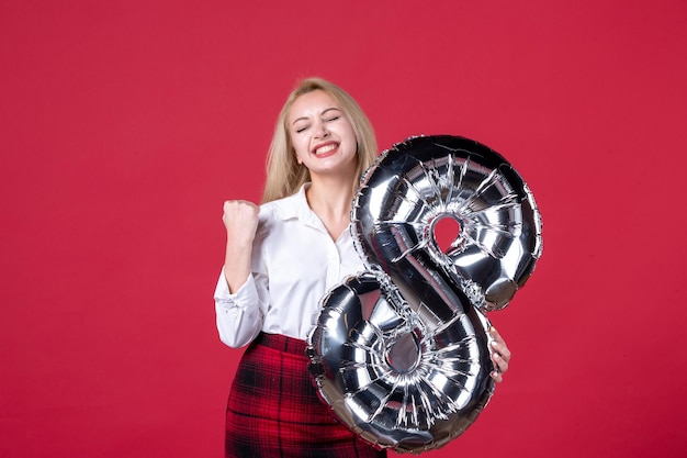 Foto vista frontal mujer joven posando con globo plateado como símbolo de marcha sobre fondo rojo igualdad feminidad femenina cariñoso día de la mujer colores sensual