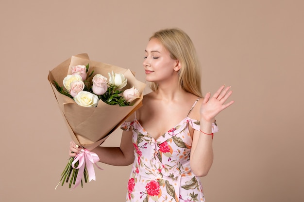 Vista frontal de la mujer joven posando con ramo de rosas hermosas en la pared marrón