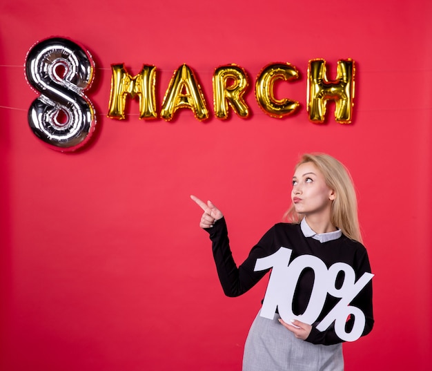 Foto vista frontal mujer joven sosteniendo la escritura con decoración de marzo sobre fondo rojo lujoso sensual igualdad femenina día de la mujer día de fiesta de salón de amor