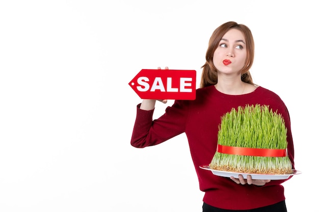 Vista frontal mujer joven sosteniendo gran semeni novruz y placa de venta sobre fondo blanco concepto de ejecutante etnia familia compras étnicos colores primaverales