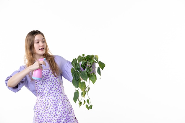 Foto vista frontal mujer joven sosteniendo maceta con planta y botella de spray sobre fondo blanco hoja jardín césped planta mujer trabajo flor