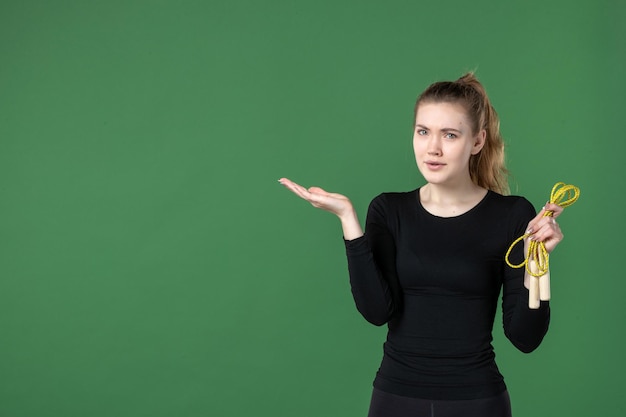 Vista frontal mujer joven sosteniendo saltar la cuerda sobre fondo verde salud mujer entrenamiento deporte gimnasia cuerpo de atleta