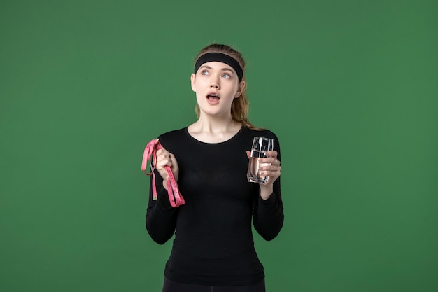 Vista frontal mujer joven con vaso de agua y medida de cintura en verde