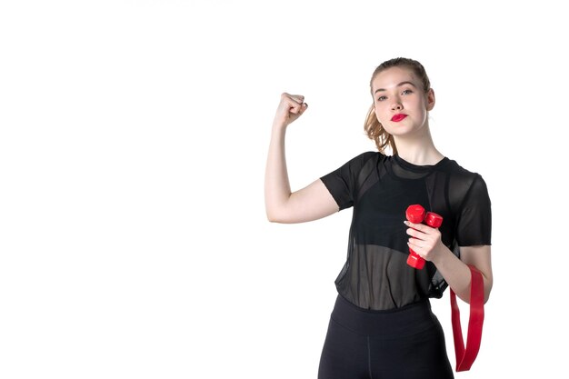 Vista frontal mujer joven con vendaje rojo y pesas sobre fondo blanco gimnasio atleta deporte estilo de vida régimen corporal entrenamiento salud