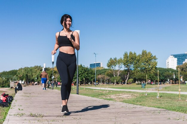 Vista frontal mujer latina trotando y sonriendo al aire libre en un espacio de copia de pasarela de madera