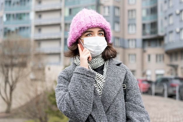 Foto vista frontal de la mujer con máscara médica en la ciudad hablando por teléfono inteligente