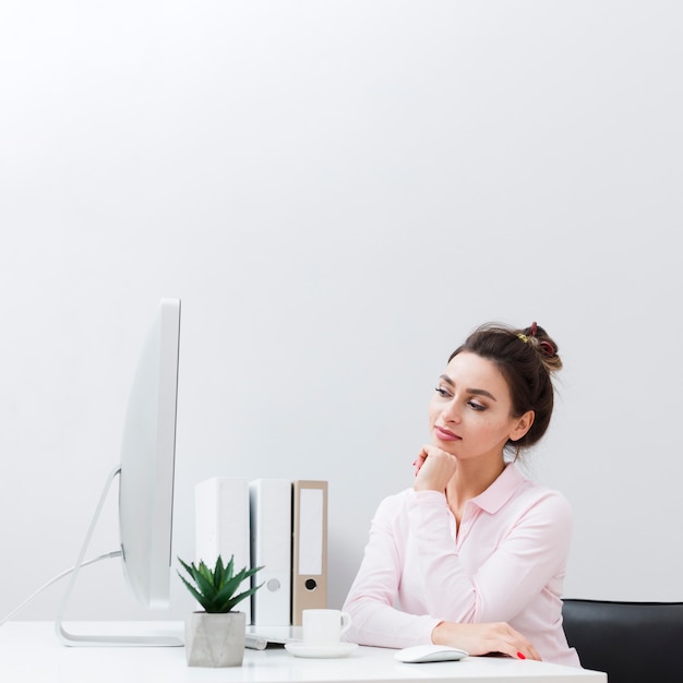 Vista frontal de la mujer pensativa en su escritorio mirando la computadora