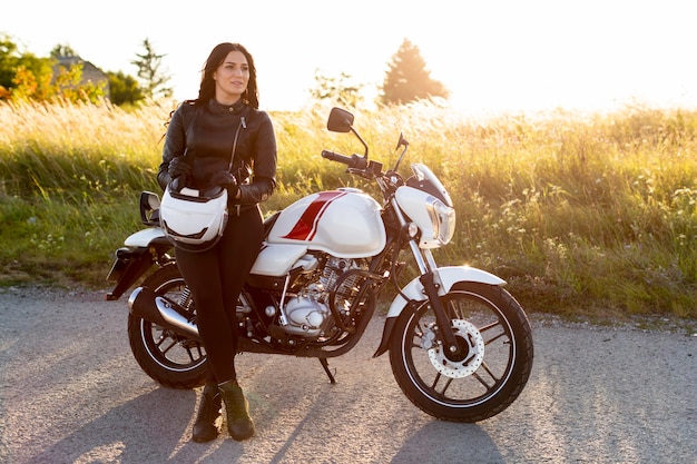 Vista frontal de la mujer posando junto a su motocicleta