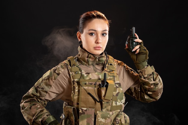 Vista frontal de la mujer soldado con granada en uniforme sobre pared negra