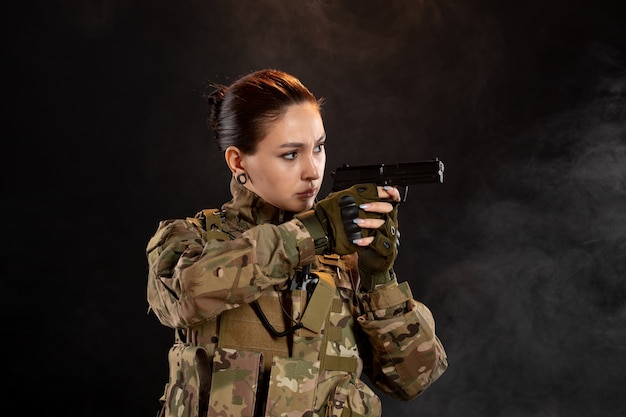 Vista frontal mujer soldado con pistola en uniforme sobre pared negra