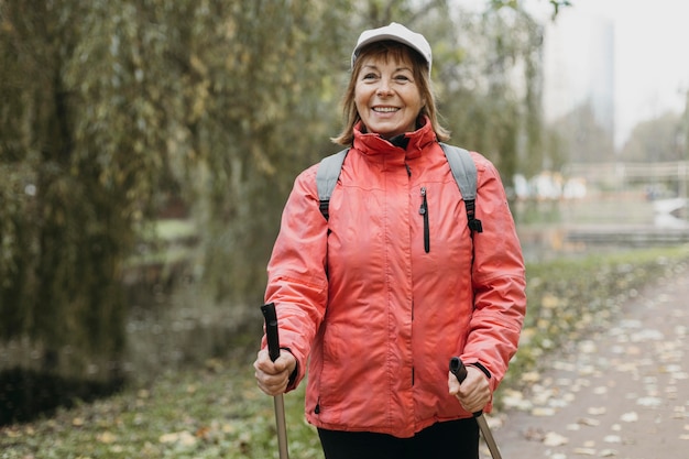 Foto vista frontal de la mujer sonriente con bastones de trekking al aire libre