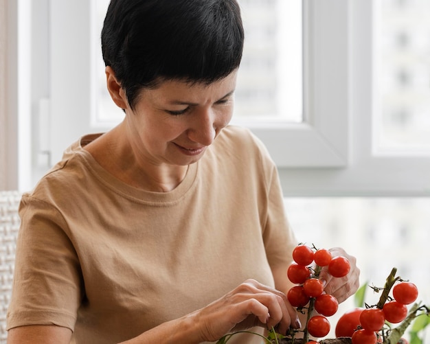 Foto vista frontal de la mujer sonriente cuidando de la planta de tomate de interior