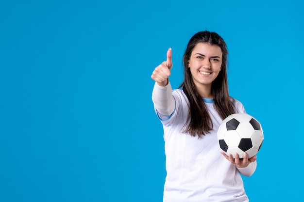 Foto vista frontal de las mujeres jóvenes con balón de fútbol en la pared azul