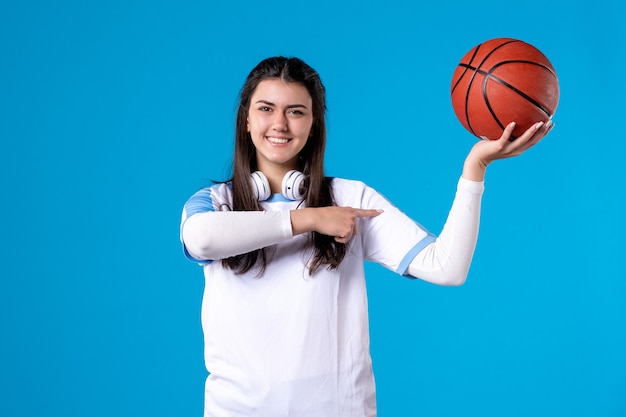 Vista frontal de las mujeres jóvenes con baloncesto en la pared azul