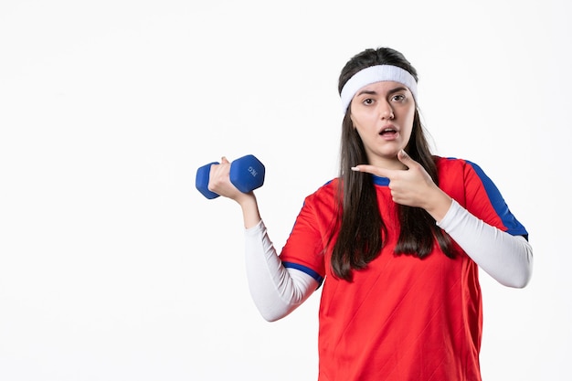 Vista frontal de las mujeres jóvenes en ropa deportiva con pesas azules en la pared blanca