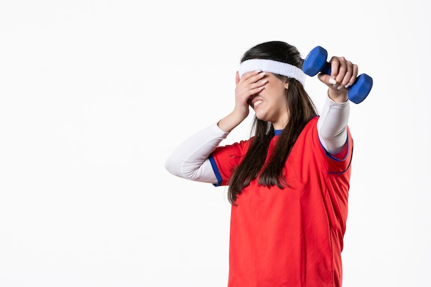 Vista frontal de las mujeres jóvenes en ropa deportiva con pesas azules en la pared blanca