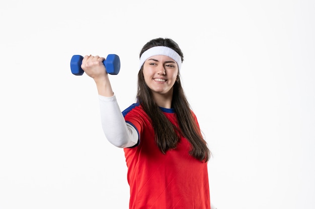 Vista frontal de las mujeres jóvenes en ropa deportiva trabajando con pesas en la pared blanca