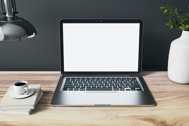 Vista frontal na tela do laptop prata moderno branco em branco com espaço para web design ou site na mesa de madeira com caneca de café vaso branco e notebooks na maquete de renderização 3D de fundo de parede escura