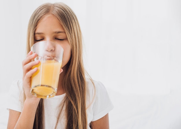 Foto vista frontal niña bebiendo jugo de naranja