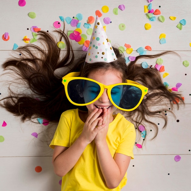 Foto vista frontal de la niña linda con grandes gafas de sol y gorro de fiesta