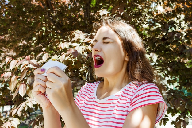 Vista frontal de una niña soltera que estornuda y sopla al aire libre con un fondo verde