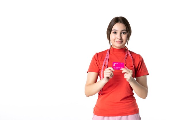Vista frontal de una niña sonriente en redorange blusa mostrando tarjeta bancaria sobre fondo blanco.