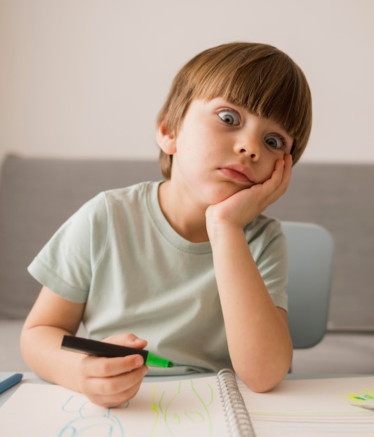 Foto vista frontal del niño aburrido en casa mientras recibe la tutoría