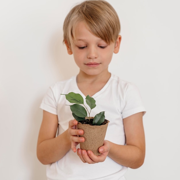 Foto vista frontal del niño con maceta de planta