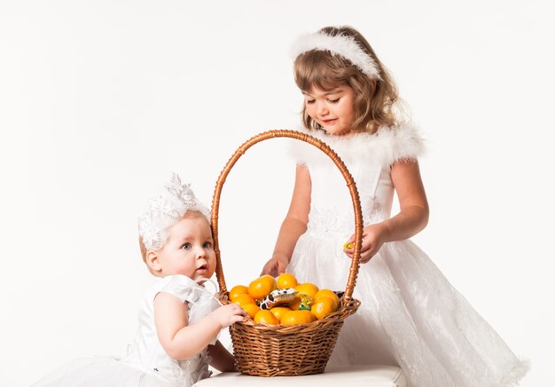 Vista frontal de niños lindos de pie junto a la canasta con naranjas y dulces.