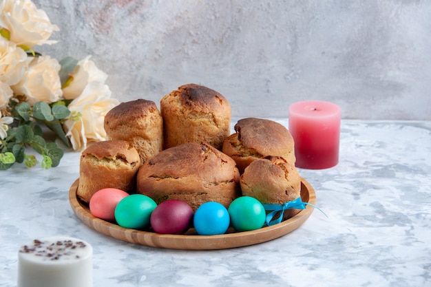 Vista frontal ovos de páscoa coloridos com pão e bolos de férias dentro da bandeja no fundo branco conceito de torta primavera ornamentado doce colorido