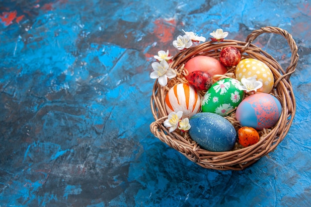 vista frontal ovos de páscoa coloridos dentro da cesta na superfície azul