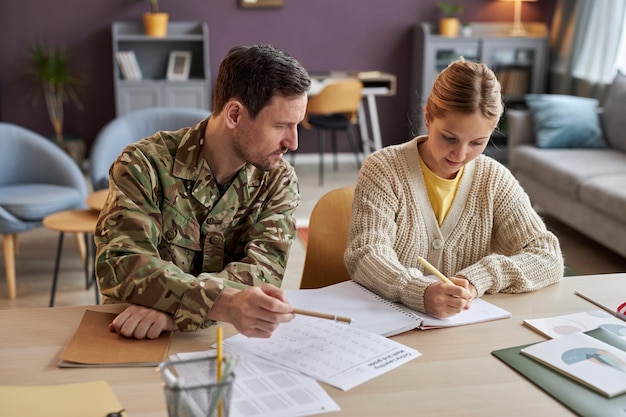 Vista frontal padre con uniforme militar ayudando a su hija con la tarea