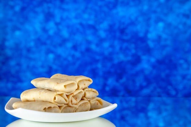 Foto vista frontal de panqueques dulces enrollados dentro de la placa sobre fondo azul comida de la mañana desayuno pastel de leche comida de azúcar de color