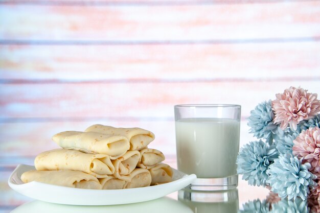 Vista frontal de panqueques dulces enrollados con un vaso de leche sobre fondo claro comida comida azúcar flor color pastel mañana