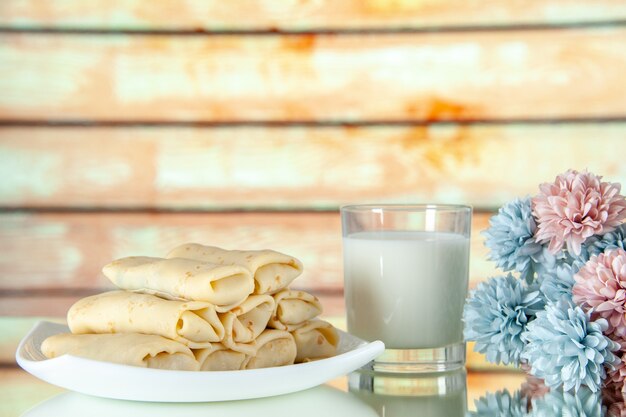 Vista frontal panqueques dulces enrollados con un vaso de leche sobre un fondo claro pastel de comida comida para el desayuno color de la flor pastel de la mañana azúcar