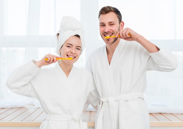 Vista frontal de la pareja en batas de baño cepillarse los dientes