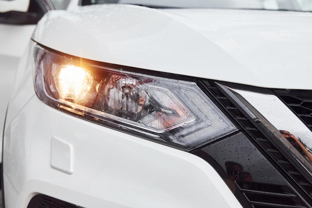 Vista frontal de partículas de automóvil moderno blanco con faros encendidos