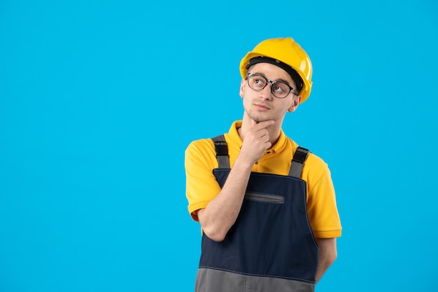 Vista frontal pensando en constructor masculino en uniforme amarillo en la pared azul