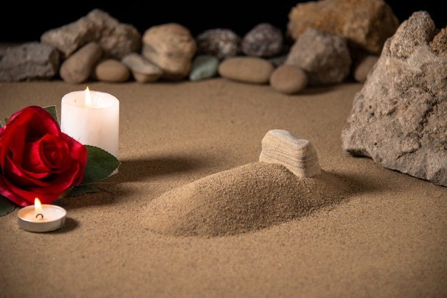 Vista frontal de la pequeña tumba con velas y piedras sobre arena.