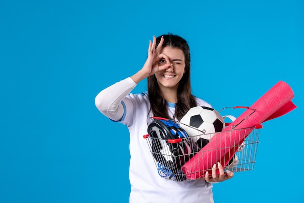 Vista frontal posando mujer joven con canasta llena de cosas deportivas azul